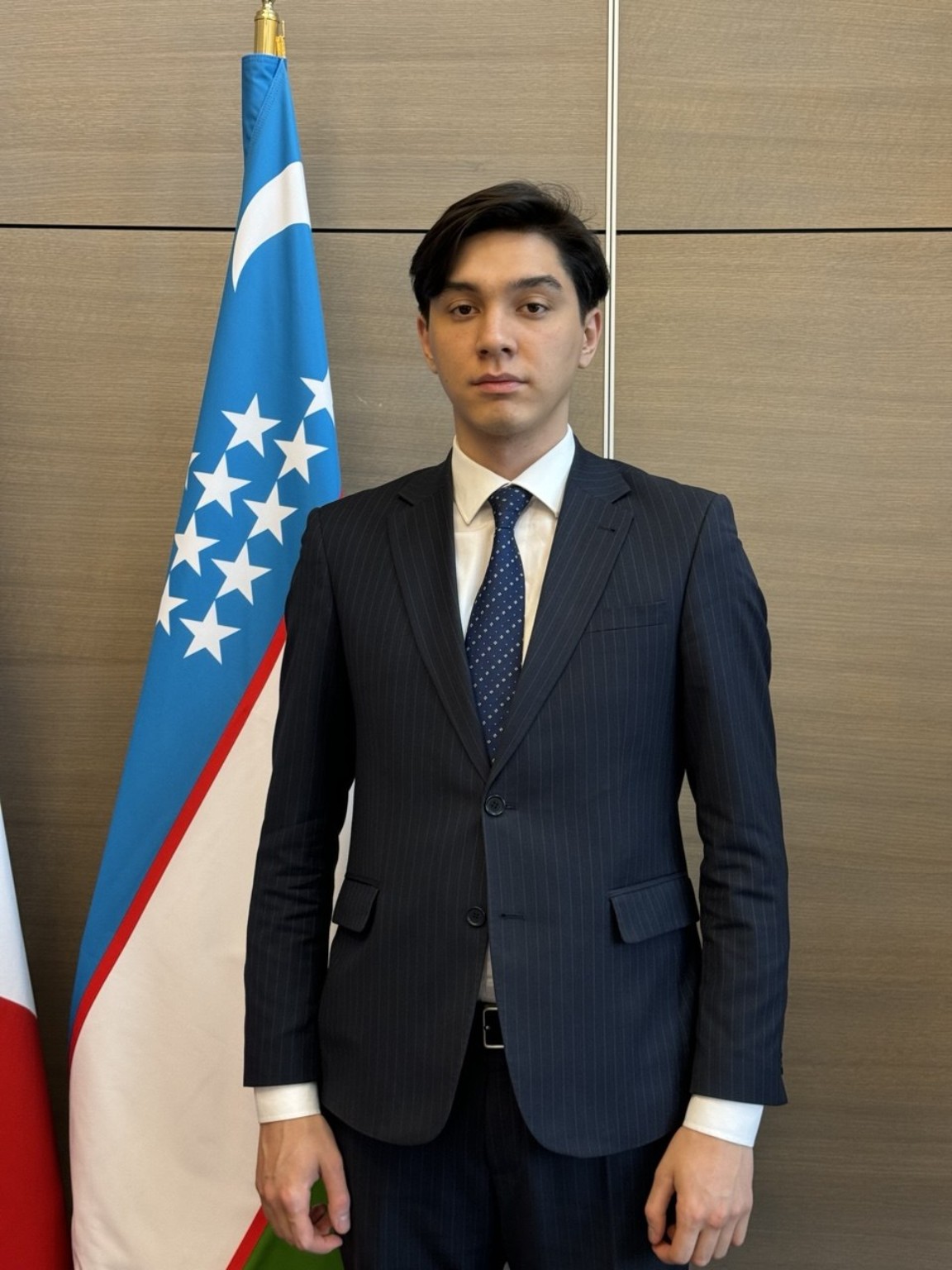 Rakhmatilla Khayrillaev beside the flag of Uzbekistan